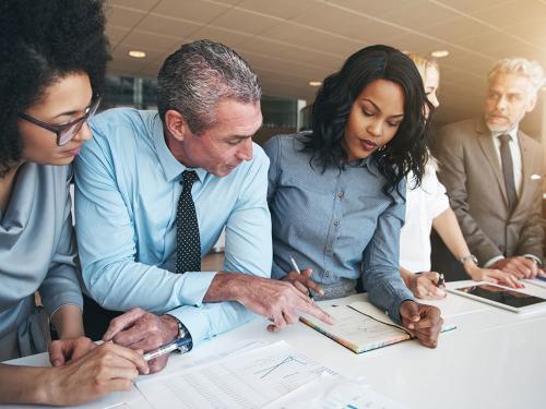 Multiracial workers discussing papers sitting in office Black and white group of people doing teamwork in contemporary office.